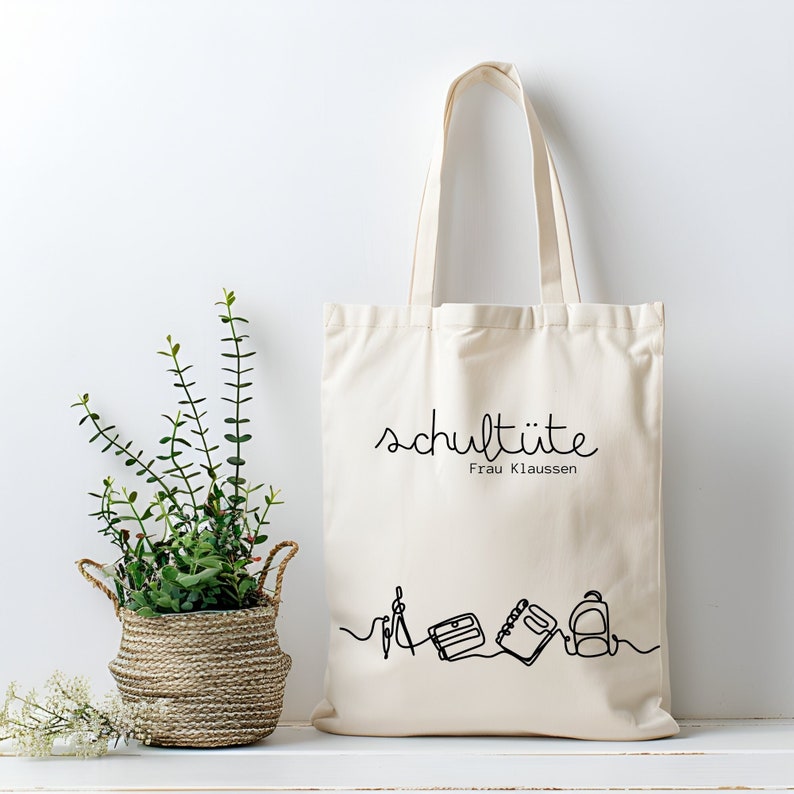 Naturfarbene Baumwolltasche mit Aufdruck schultüte und dem Namen der Lehrkraft, mit einer Illustration von Schul-, oder Berufsutensilien, wie Notizheft und Rucksack. Personalisierte Tasche.