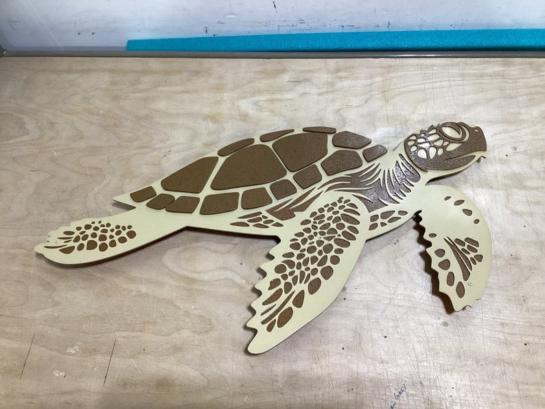 May include: A beige wooden cutout of a sea turtle with a brown shell. The turtle is facing right and has a detailed design.