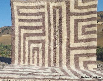 May include: A large, white and brown geometric patterned rug with a fringe border. The rug is made of wool and has a soft, fluffy texture. The rug is laid out on a bed of gravel.