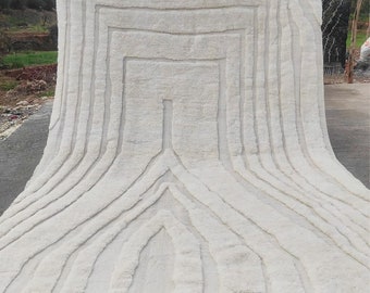 May include: A white, hand-woven rug with a geometric pattern. The rug has a fringe border and is made of wool.