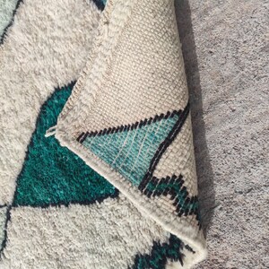 May include: A white and green Moroccan rug with a geometric pattern. The rug is folded in half, showing the fringe on the edge.