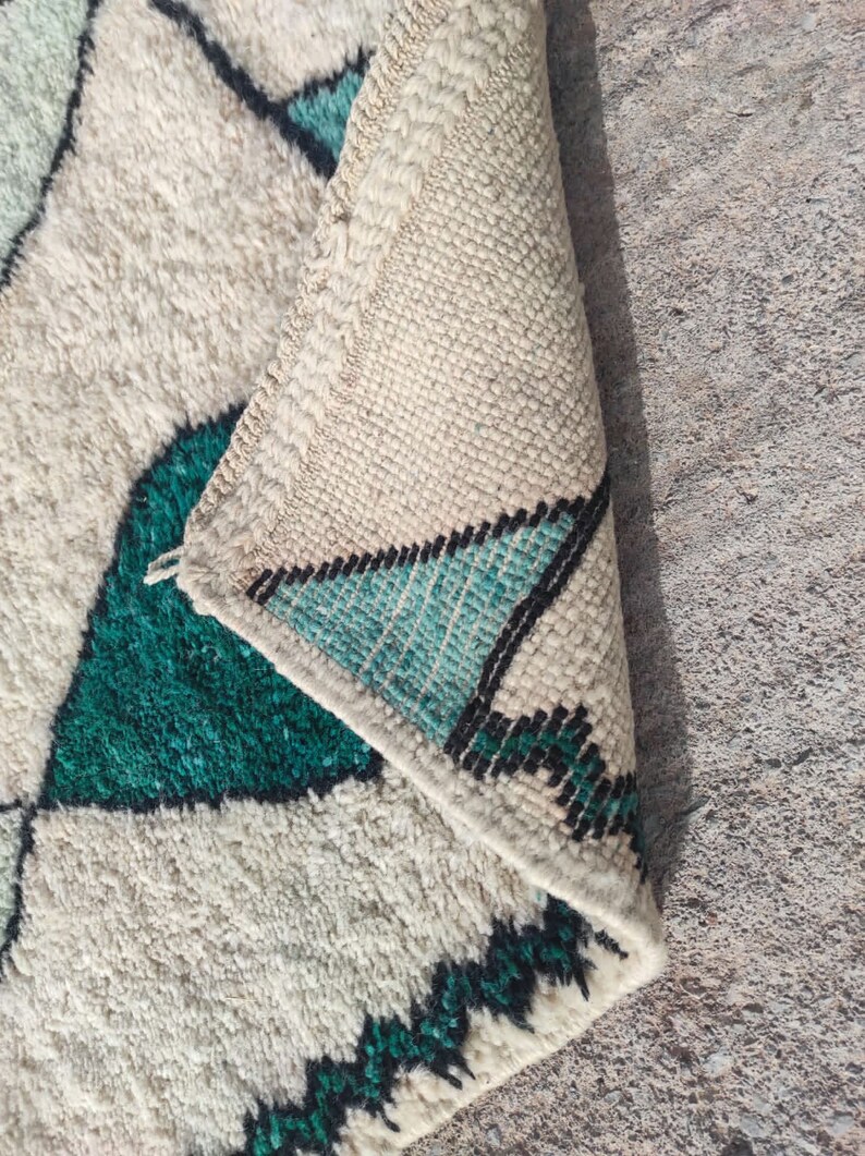 May include: A white and green Moroccan rug with a geometric pattern. The rug is folded in half, showing the fringe on the edge.