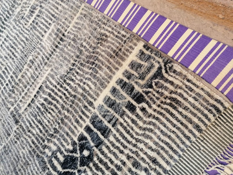 May include: A black and white patterned rug with a purple and white striped border. The rug has a fringe on the bottom edge.