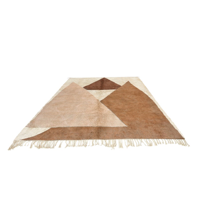 Puede incluir: Una alfombra geom&eacute;trica con fondo blanco y tri&aacute;ngulos marrones y beige. La alfombra tiene un borde de flecos.