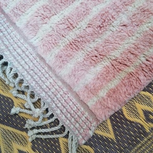 May include: Pink and white striped rug with a fringed border. The rug is made of a soft, fluffy material.