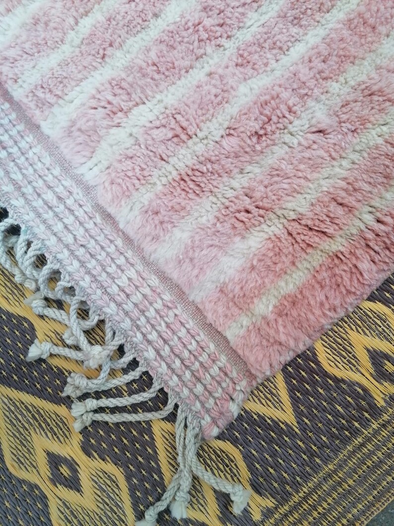 May include: Pink and white striped rug with a fringed border. The rug is made of a soft, fluffy material.
