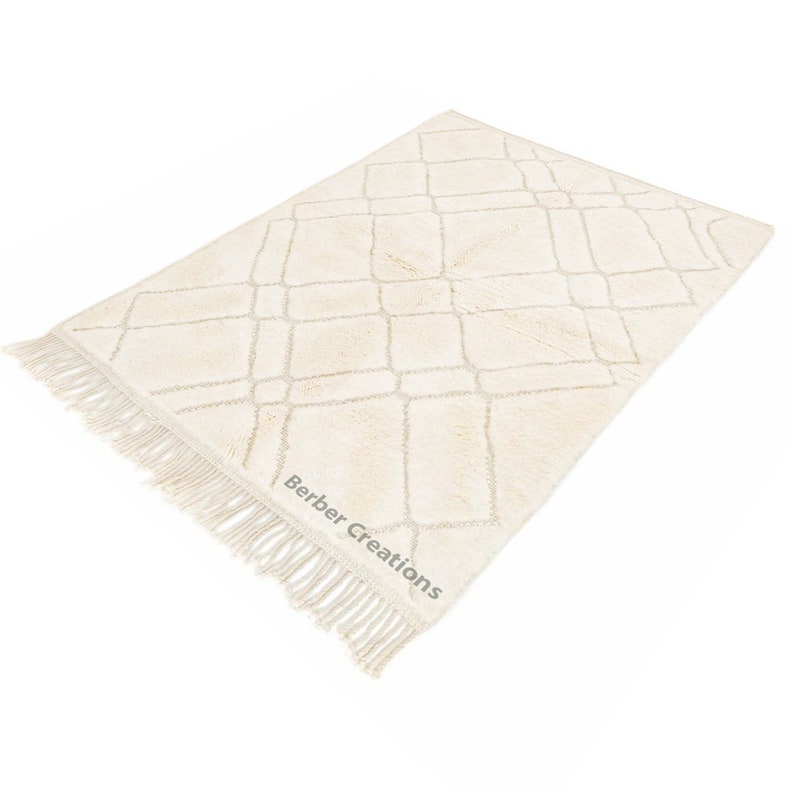 May include: A cream-colored rug with a diamond pattern and fringe. The rug has a subtle texture and is made of a soft material. The rug is labeled "Berber Creations".