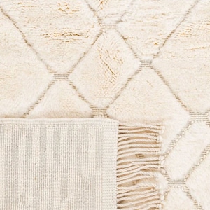 May include: A cream-colored rug with a diamond pattern and fringe. The rug is made of a soft, fluffy material.