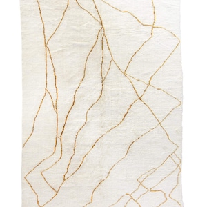 Könnte beinhalten: Ein weißer Teppich mit einem geometrischen Muster aus dünnen goldenen Linien. Der Teppich hat einen Fransenrand.