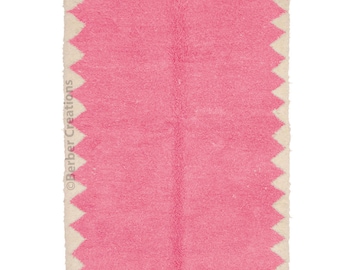 May include: A pink and white Moroccan rug with a geometric pattern. The rug has a fringe border.