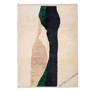 Pu&ograve; includere: Un tappeto beige con un designo astratto in nero e verde. Il tappeto ha un bordo a frangia e il testo "Berber Creations" &egrave; stampato nell'angolo in basso a destra.