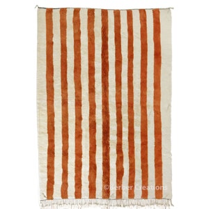 May include: A white and orange striped rug with fringe on the bottom. The rug has a traditional Moroccan design.