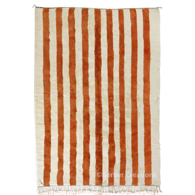 May include: A white and orange striped rug with fringe on the bottom. The rug has a traditional Moroccan design.