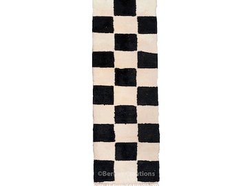 May include: Black and white checkered rug with fringe. The rug is made of wool and has a traditional Moroccan design.