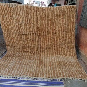 Puede incluir: Una alfombra grande, rectangular, de color marr&oacute;n y crema con un patr&oacute;n tejido. La alfombra tiene un borde de flecos.