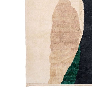 Pu&ograve; includere: Primo piano di un tappeto con forme astratte in beige, nero e verde. Il tappeto ha un bordo con frange.