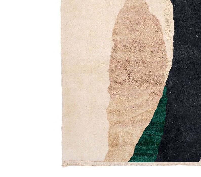 Pu&ograve; includere: Primo piano di un tappeto con forme astratte in beige, nero e verde. Il tappeto ha un bordo con frange.