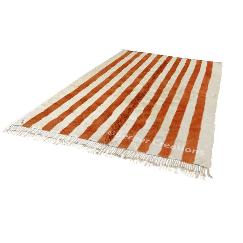 May include: A white and orange striped rug with fringe on the edges. The rug is made of wool and has a traditional Moroccan design.
