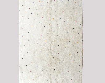 May include: A white Moroccan rug with a scattered pattern of colorful dots. The rug has a fringe border.