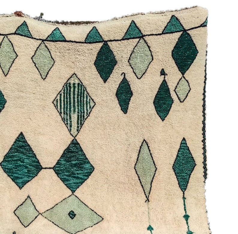 May include: A cream-colored rug with a geometric pattern of green and white diamonds. The rug has a fringe border.