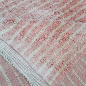 May include: Pink and white striped rug with a fringed border. The rug is made of a soft, fluffy material.
