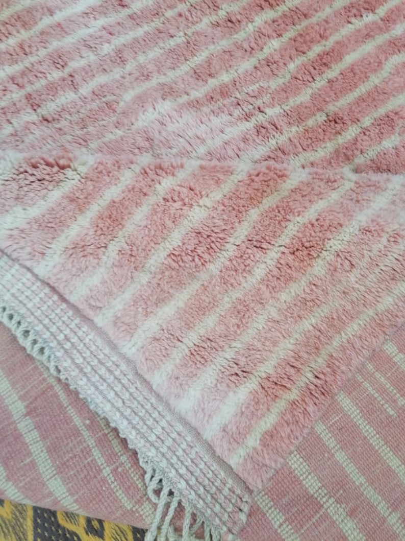 May include: Pink and white striped rug with a fringed border. The rug is made of a soft, fluffy material.