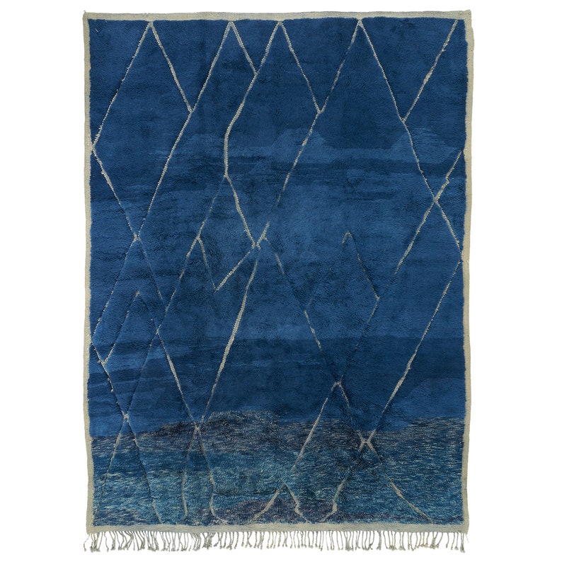 May include: A blue and white Moroccan rug with a geometric pattern. The rug has a fringe border.