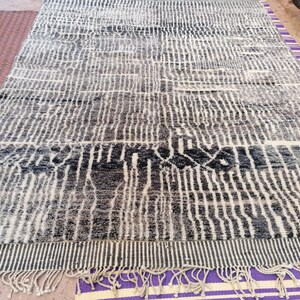 May include: A black and white patterned rug with a fringe border. The rug has a geometric design with vertical lines and a wavy pattern.