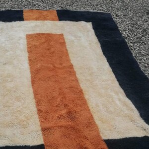 K&ouml;nnte beinhalten: Ein rechteckiger Teppich mit geometrischem Muster. Der Teppich hat einen schwarzen Rand, eine wei&szlig;e Mitte und einen braunen Streifen in der Mitte.