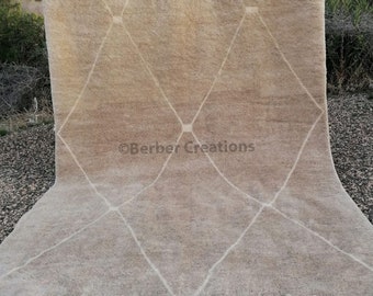 May include: A beige and white Moroccan rug with a diamond pattern. The rug has a fringe border and is made of wool.