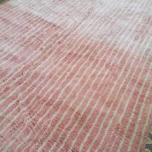 May include: A pink and white striped rug with a fluffy texture. The rug has a gradient pattern, with the pink colour being more prominent at the bottom and the white colour being more prominent at the top.