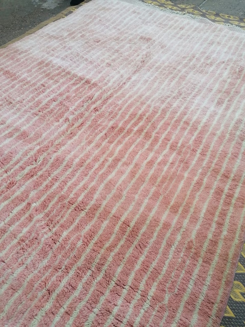 May include: A pink and white striped rug with a fluffy texture. The rug has a gradient pattern, with the pink colour being more prominent at the bottom and the white colour being more prominent at the top.