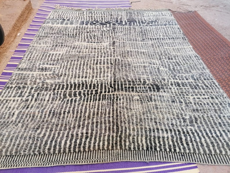 May include: A black and white striped rug with a geometric pattern. The rug is made of wool and has a soft, fluffy texture.