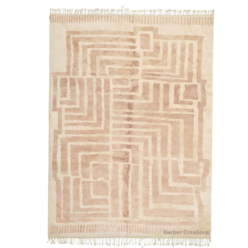 Puede incluir: Una alfombra beige con un patr&oacute;n geom&eacute;trico en un tono beige m&aacute;s claro. La alfombra tiene un borde de flecos y el texto "Berber Creations" est&aacute; impreso en la esquina inferior derecha.