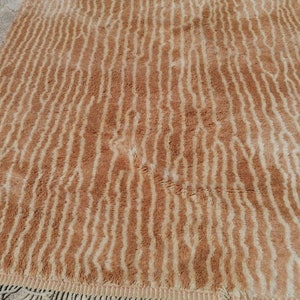 Puede incluir: Una alfombra de pelo marr&oacute;n y crema con un patr&oacute;n ondulado a rayas. La alfombra tiene un borde de flecos.