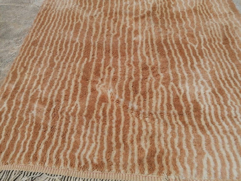 Puede incluir: Una alfombra de pelo marr&oacute;n y crema con un patr&oacute;n ondulado a rayas. La alfombra tiene un borde de flecos.