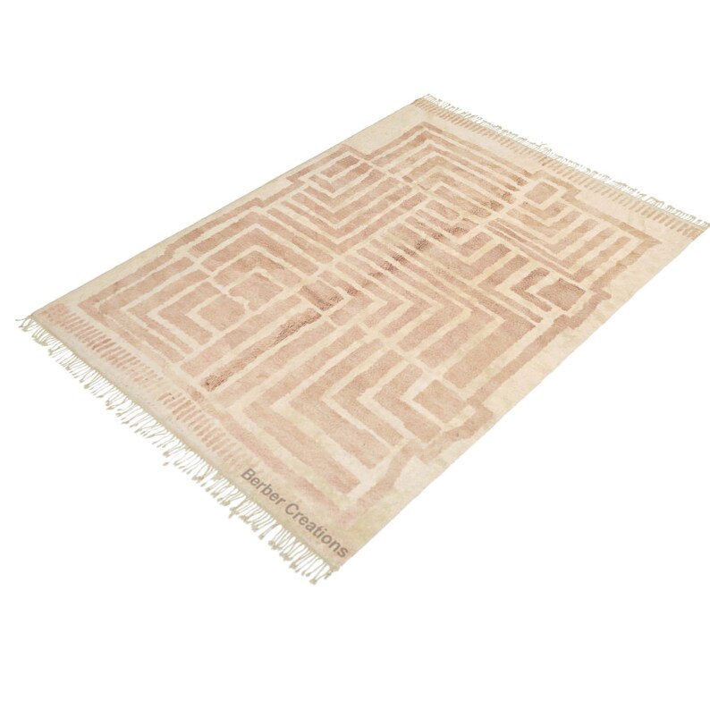Puede incluir: Una alfombra beige con un patr&oacute;n geom&eacute;trico marr&oacute;n que se asemeja a un laberinto. La alfombra tiene flecos en todos los lados y el texto "Barber Creations" est&aacute; impreso en la esquina inferior derecha.