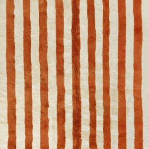May include: A close-up of a rug with alternating stripes of white and orange. The rug has a fuzzy texture.