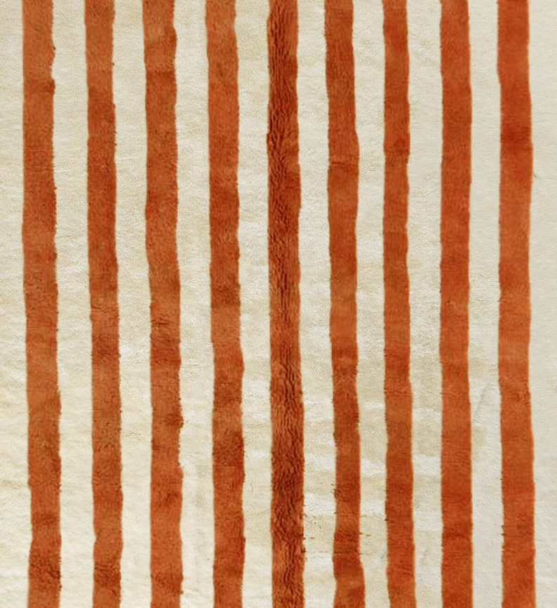 May include: A close-up of a rug with alternating stripes of white and orange. The rug has a fuzzy texture.