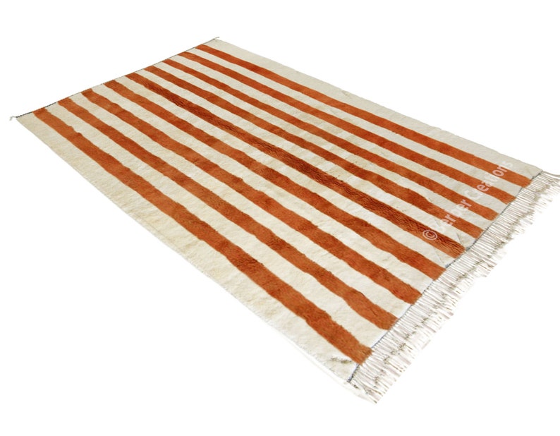 May include: A white and orange striped rug with fringe on the edges. The rug has a woven texture.