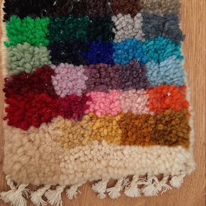 Op de afbeelding: Een kleurrijk tapijt met een verscheidenheid aan kleuren, waaronder zwart, groen, blauw, rood, roze, geel en oranje. Het tapijt heeft een franje rand en is gemaakt van een zacht, pluche materiaal.