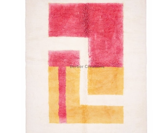 Könnte beinhalten: Ein weißer Teppich mit einem geometrischen Muster in Rosa und Gelb. Das Muster besteht aus einer Reihe von Quadraten und Rechtecken.
