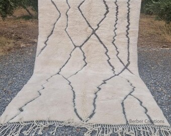 Könnte beinhalten: Ein weißer und schwarzer marokkanischer Teppich mit geometrischem Muster. Der Teppich hat einen Fransenrand und ist aus Wolle.