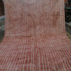 May include: A pink and white striped rug with a fringe border. The rug is made of wool and has a soft, fluffy texture.