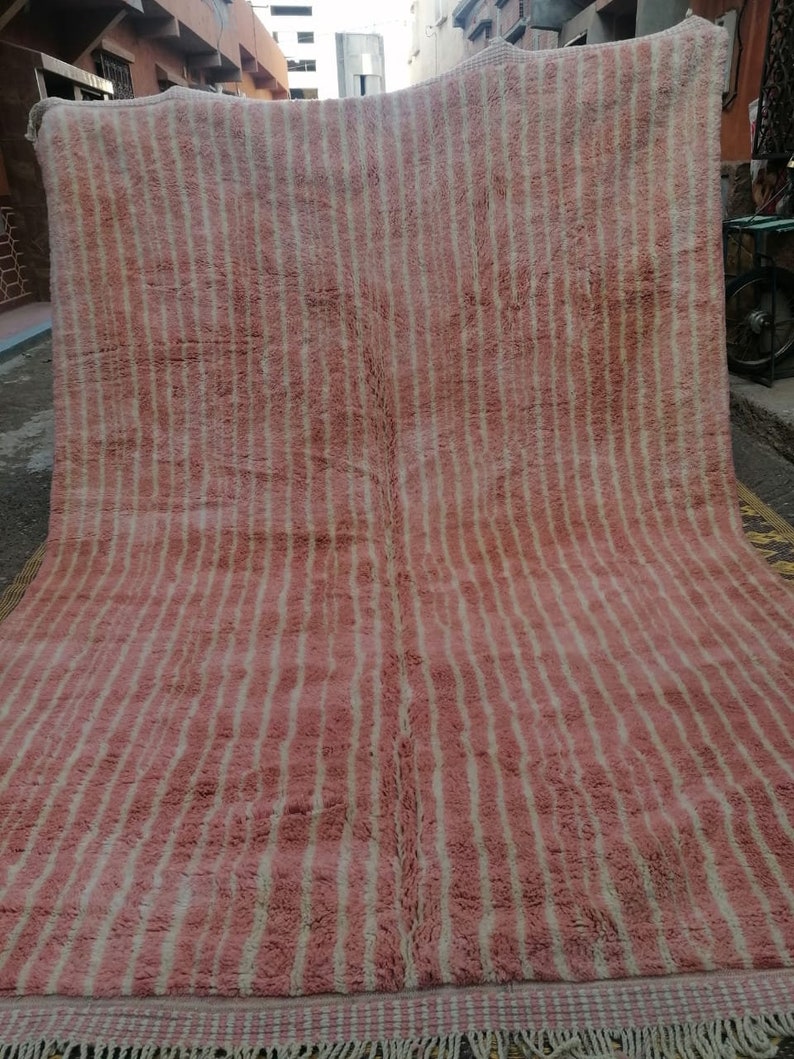 May include: A pink and white striped rug with a fringe border. The rug is made of wool and has a soft, fluffy texture.
