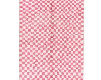 May include: A pink and white checkered rug with a fringe border. The rug has a geometric pattern and is made of a soft, fluffy material.