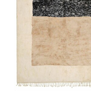 May include: A beige and black area rug with a fringe border. The rug has a geometric design with a large beige rectangle in the centre and a smaller black rectangle above it.