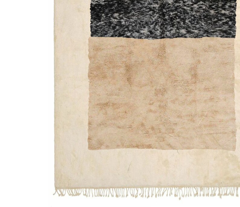 May include: A beige and black area rug with a fringe border. The rug has a geometric design with a large beige rectangle in the centre and a smaller black rectangle above it.