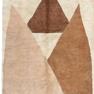 Puede incluir: Una alfombra geom&eacute;trica beige, marr&oacute;n y blanca con un dise&ntilde;o moderno. La alfombra presenta un tri&aacute;ngulo grande en el centro con dos tri&aacute;ngulos m&aacute;s peque&ntilde;os a cada lado.