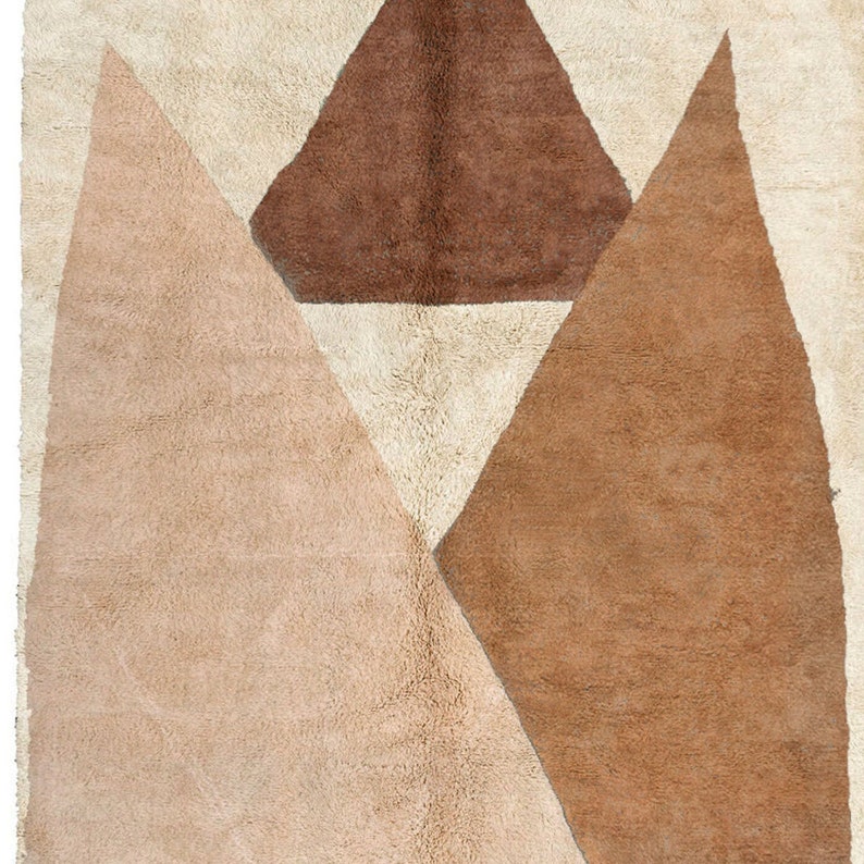 Puede incluir: Una alfombra geom&eacute;trica beige, marr&oacute;n y blanca con un dise&ntilde;o moderno. La alfombra presenta un tri&aacute;ngulo grande en el centro con dos tri&aacute;ngulos m&aacute;s peque&ntilde;os a cada lado.